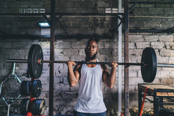 Strong black man lifting heavy barbell in gym