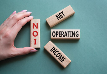 NOI - Net Operating Income symbol. Concept word NOI on wooden cubes. Businessman hand. Beautiful...