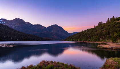 Fototapeta premium lake surrounded by forested mountains under a purple sky at sunset