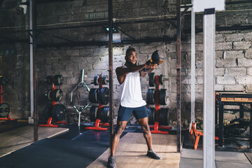 Muscular man standing and swinging heavy kettlebell in gym