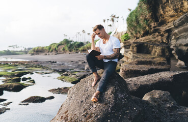 Young man sitting on rock by river and reading book