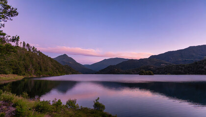 lake surrounded by forested mountains under a purple sky at sunset