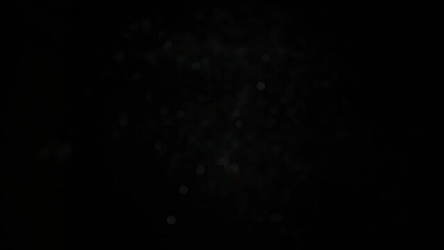 Silver glitter flying after being exploded, bright sparkles bouncing against camera flying and falling down on black background. Top view close up macro slow motion