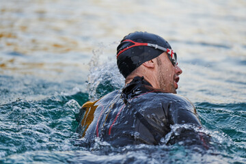 Triathlon athlete swimming on lake in sunrise wearing wetsuit