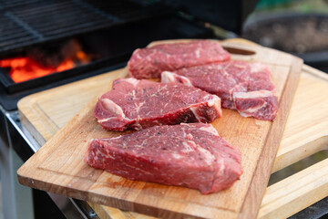 Four beef steaks lie on a cutting board next to the grill