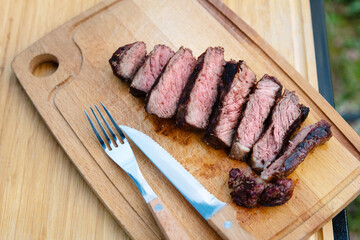 Top view of beef steak on a cutting board, which is cut into pieces. You can see the cut and the degree of readiness of the meat. A knife and fork lie nearby.
