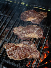Three ribeye steaks are cooked on a charcoal grill on a cast iron grate