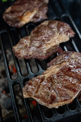 Three ribeye steaks are cooked on a charcoal grill on a cast iron grate