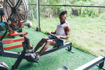 Obraz premium Strong black sportsman resting on bench while pulling cable in gym