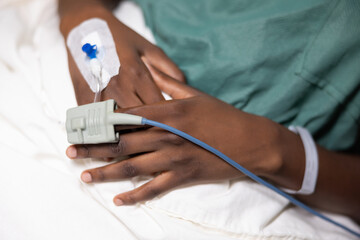 Close-up: African woman's hands with a fingertip oximeter and a thin catheter from drip.