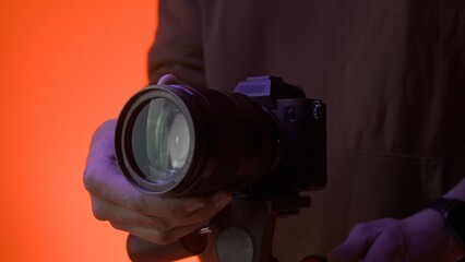Professional photo camera stands on a tripod in a studio with color neon lighting. The photographer makes settings before shooting begins.