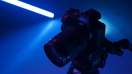 Professional photo camera stands on a tripod in a studio with color neon lighting.