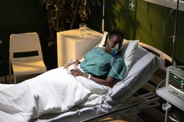 Woman lying in bed, African, with oxygen mask, looking at the ceiling.