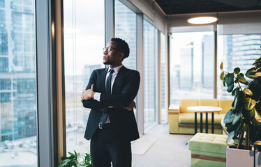 Confident black businessman in suit standing near glass wall