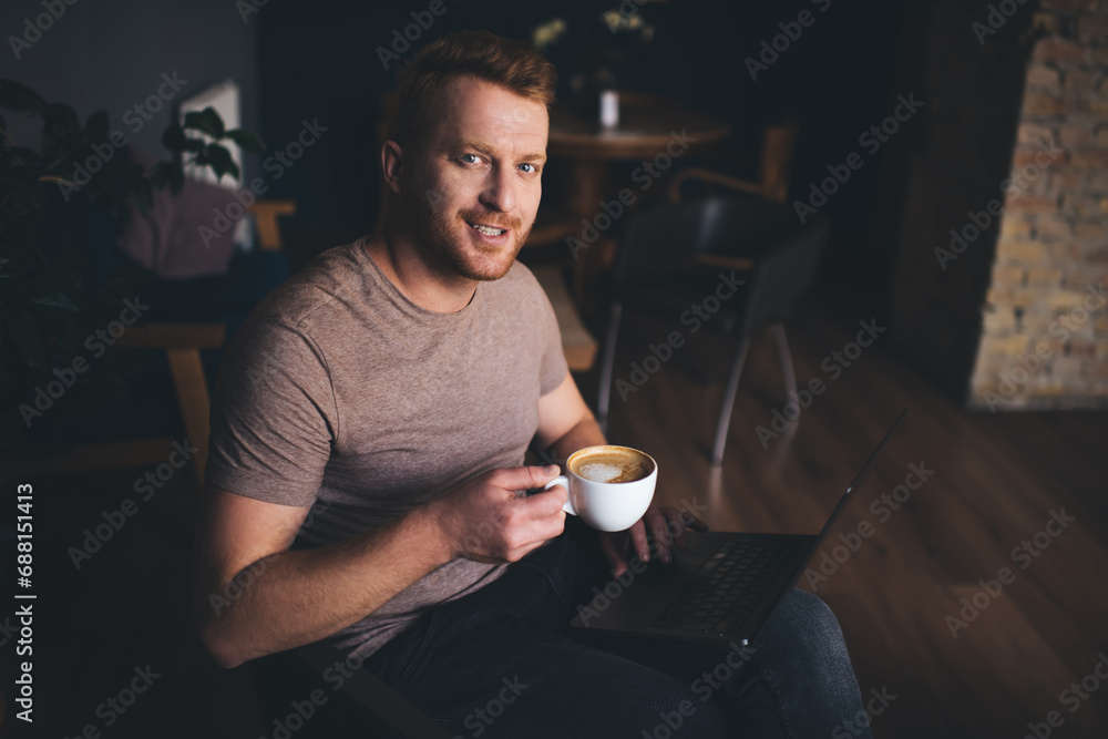 Poster portrait of skilled freelancer with coffee cup smiling at camera during time for remote working in c
