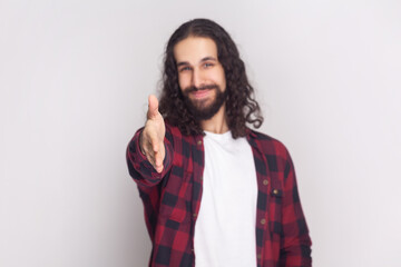 Man with long curly hair in checkered red shirt gives handshake, greets with someone, smiles...