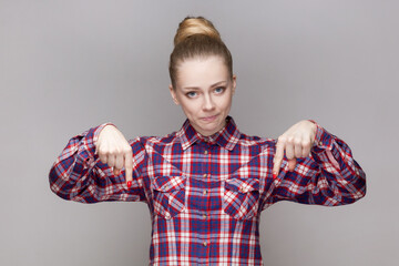 Here and right now. Portrait of serious bossy beautiful woman with bun hairstyle pointing down with...