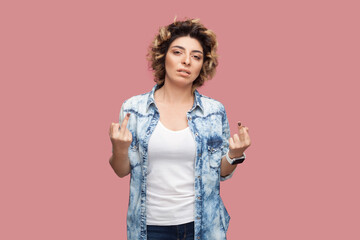 Portrait of rude impolite serious woman with curly hairstyle wearing blue shirt standing with middle fingers, arguing with somebody. Indoor studio shot isolated on pink background. - obrazy, fototapety, plakaty