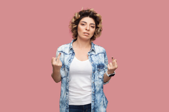 Portrait of rude impolite serious woman with curly hairstyle wearing blue shirt standing with middle fingers, arguing with somebody. Indoor studio shot isolated on pink background.