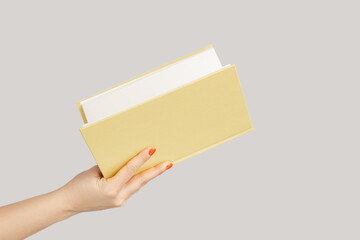 Closeup of woman hand holding open book or organizer. Indoor studio shot isolated on gray...