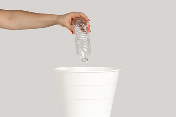 Closeup of woman hand throwing away empty plastic bottle, saving environment, recycle. Indoor studio shot isolated on gray background.