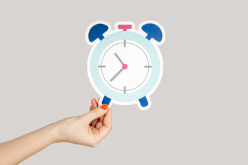 Closeup of woman hand holding paper clock, alarm, paper craft, showing time. Indoor studio shot...