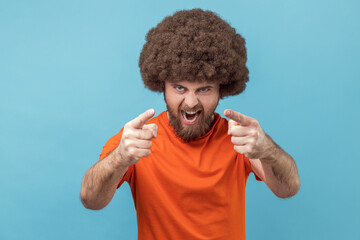 Portrait of angry man with Afro hairstyle wearing orange T-shirt pointing finger at camera choosing...
