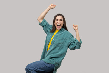 Victorious delighted happy woman raising hands, shouting for joy, screaming celebrating win success, thrilled emotions, wearing casual style jacket. Indoor studio shot isolated on gray background.