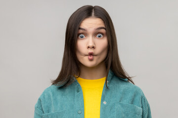 Portrait of attractive childish dark haired woman fooling around making fish lips, having fun, humor, wearing casual style jacket. Indoor studio shot isolated on gray background.