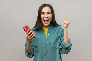 Happy satisfied woman holding smartphone and smiling making yes gesture, celebrating online lottery...