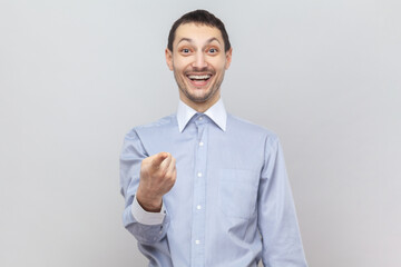 Portrait of smiling optimistic joyful attractive man standing looking at camera with toothy smile, pointing at you, wearing light blue shirt. Indoor studio shot isolated on gray background.