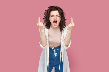 Portrait of rude impolite woman with curly hair wearing casual style outfit standing showing middle fingers, screaming with hate and anger. Indoor studio shot isolated on pink background. - obrazy, fototapety, plakaty