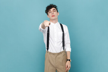 Portrait of serious strict young attractive man wearing white shirt and suspender, pointing at...