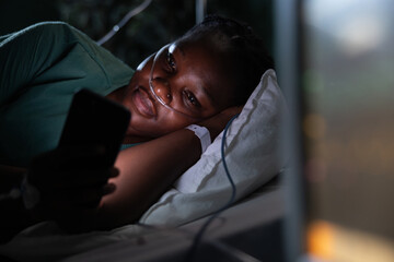 Patient in hospital room lies on her side, using the phone to watch videos.