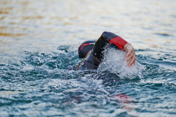 Triathlon athlete swimming on lake in sunrise wearing wetsuit - 688153626