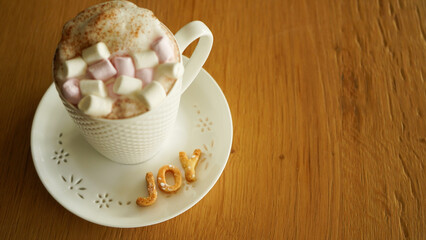 cup of hot chocolate with marshmallows on a saucer with cookies in the shape of letters with the written phrase Joy.