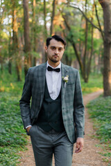 Beautiful couple, the groom in a green suit and the bride in an unusual pink wedding dress, posing at a luxurious ceremony with beautiful decor and an arch with a chandelier and candles in the forest 