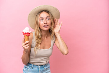 Young Russian woman holding an ice cream isolated on pink background listening to something by...
