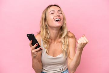 Young Russian woman isolated on pink background using mobile phone and doing victory gesture