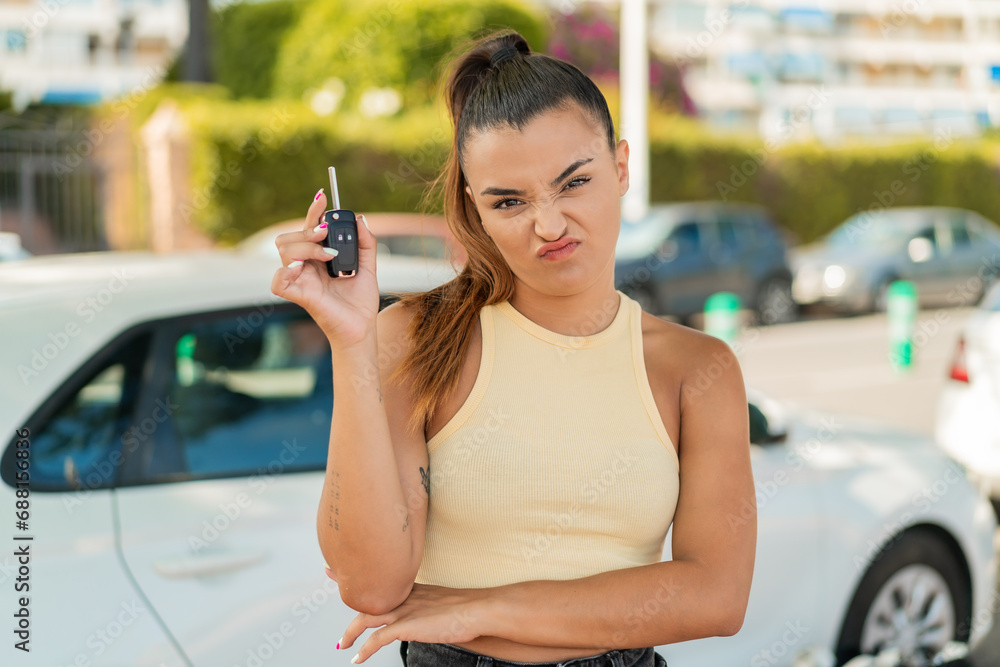 Wall mural Young pretty woman holding car keys at outdoors with sad expression