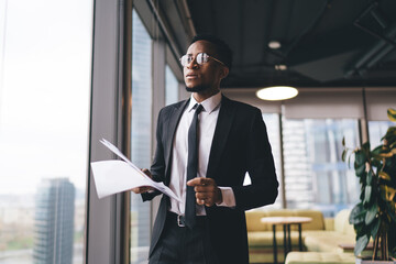 Black entrepreneur with papers in workplace - obrazy, fototapety, plakaty