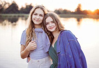 Summer portrait of two teenagers girl friends on wooden bridge at nature outdoors. - obrazy, fototapety, plakaty
