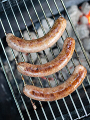 Meat sausages are cooked on a grill over coals