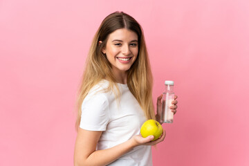 Young blonde woman isolated on pink background with an apple and with a bottle of water
