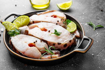 Raw catfish steaks with herbs, lime and spices in a baking dish on a gray background