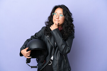 Young asian woman with a motorcycle helmet isolated on purple background having doubts and thinking