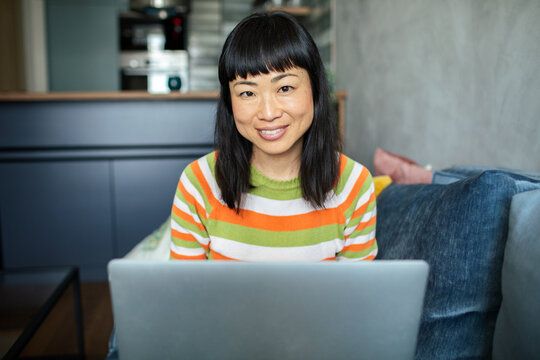 Woman sitting on couch with laptop looking at camera