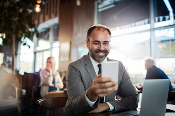 Happy businessman sitting in cafe using smartphone