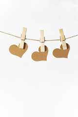Three hearts hanging from hemp rope held in place with wooden clothespin. Love card. White background. Vertical.