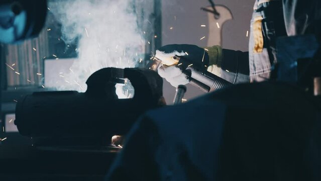 Welding in the Engineering Workshop. Welding sparks, slow motion. A worker uses a welding machine. Close up of a welding machine in work. Worker welds metal. Macro. 4K